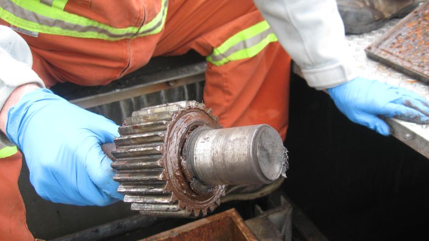 A damaged metal pipe with a gear around it, held by a gloved hand