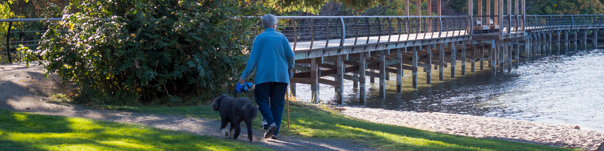 Woman walking dog on trail at Crofton Beach Park with seawalk in the background