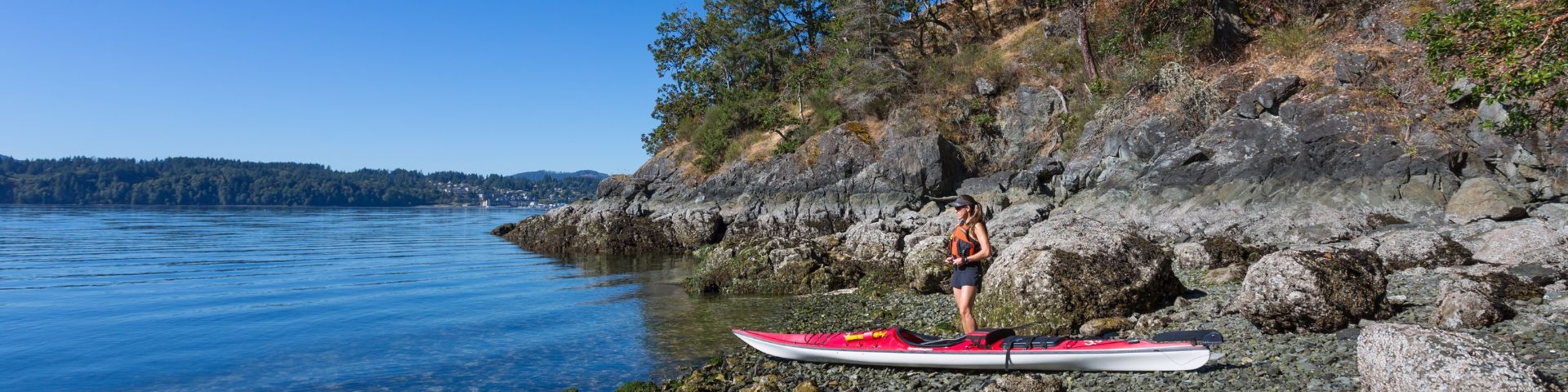 Kayaker standing on ocean shore with bright blue sky in background